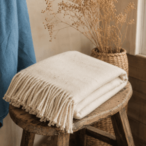 Plaid écru en laine artisanale avec franges posé sur un tabouret en boi